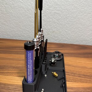 May include: A black plastic tool organizer with a variety of tools, including screwdrivers, a small tube of lubricant, and a few small parts. The organizer has a compartment for each tool and a small tray for the parts.