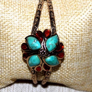 May include: A gold-tone bangle bracelet with a turquoise and red stone flower design.