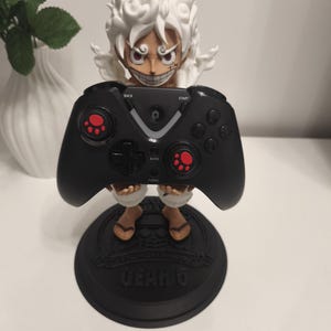 May include: A figurine of a character with spiky white hair and a wide grin, holding a black video game controller. The controller features red paw-print accents on the joysticks. The figurine stands on a black circular base labeled GEAR 5.