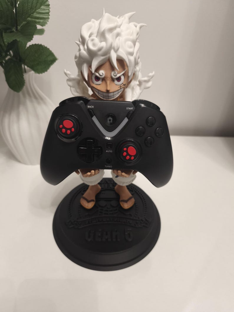 May include: A figurine of a character with spiky white hair and a wide grin, holding a black video game controller. The controller features red paw-print accents on the joysticks. The figurine stands on a black circular base labeled GEAR 5.