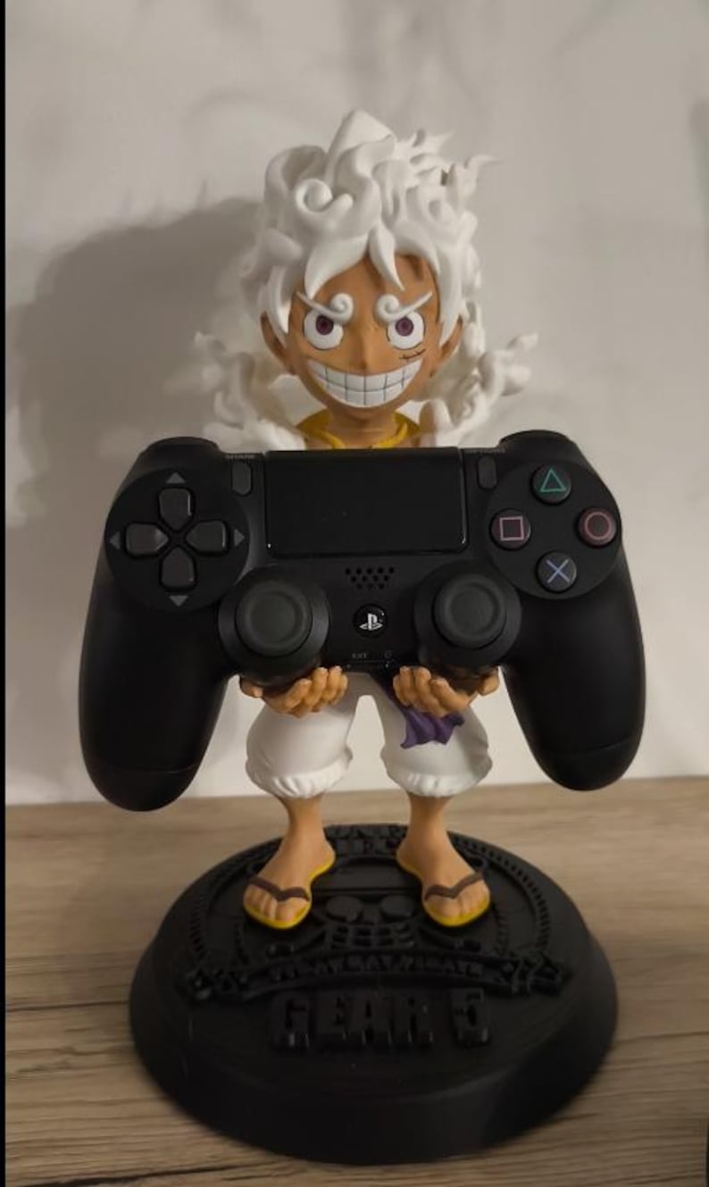 May include: A black video game controller held by a figurine of a character with spiky white hair and a wide grin. The figure wears white shorts and stands on a round black base with the text GEAR 5 embossed on the front of the circular stand.