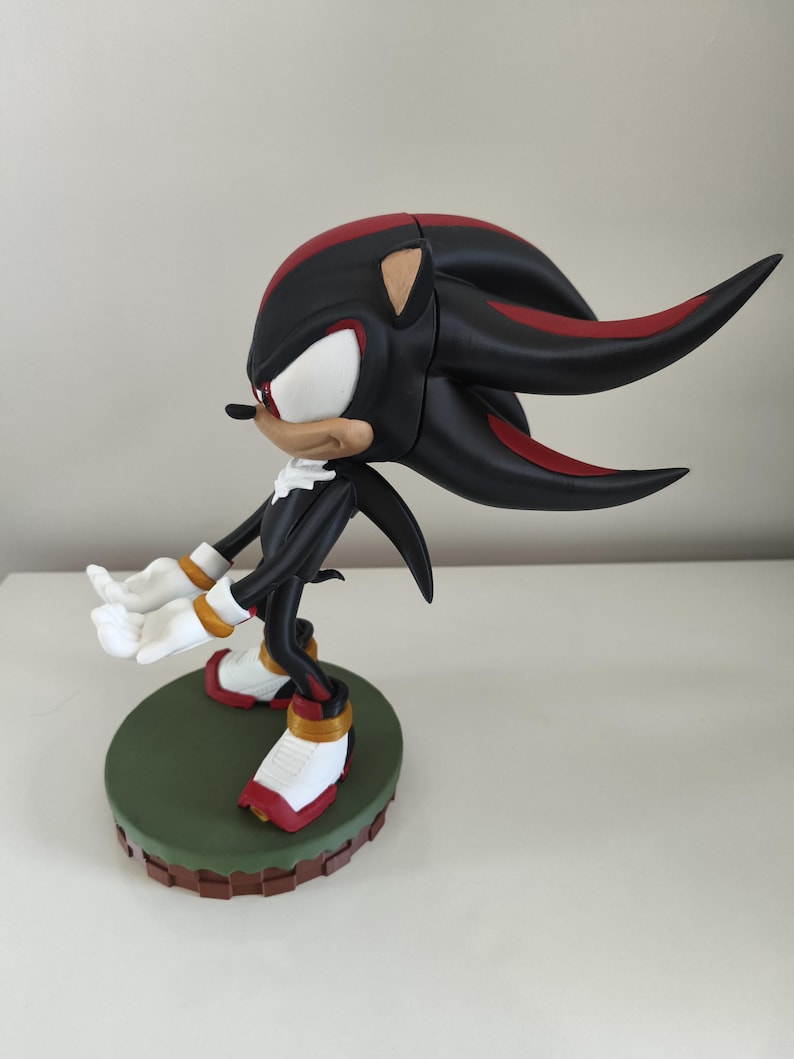 Peut inclure: Figurine noire et rouge d'un personnage avec des gants et des chaussures blancs, debout sur une base verte. Le personnage a un visage blanc, un museau beige et des &eacute;pines rouges et noires. La figurine est pos&eacute;e avec les bras tendus.
