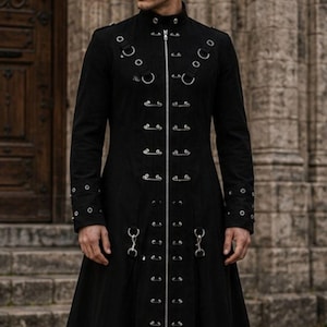 May include: A long black coat featuring a full-length front zip, a high collar, and multiple silver-toned metal eyelets and rings arranged in vertical rows along the chest and cuffs. The garment has a structured fit and a flared hemline.
