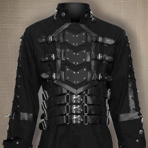 May include: Black long-sleeved jacket with a black leather harness and buckles. The harness has a decorative design with studs and straps.