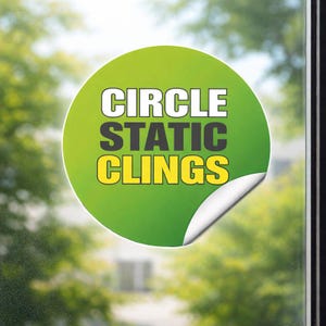 Puede incluir: Una pegatina estática circular, verde y amarilla, con las palabras "CIRCLE STATIC CLINGS" en blanco y amarillo. La pegatina está parcialmente despegada, revelando una capa adhesiva blanca. El fondo es una vista borrosa de árboles.