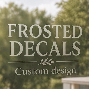 May include: White text on a frosted surface reads "FROSTED DECALS" above "Custom design". A decorative line with leaf accents separates the phrases. The background is a blurred view of green foliage.