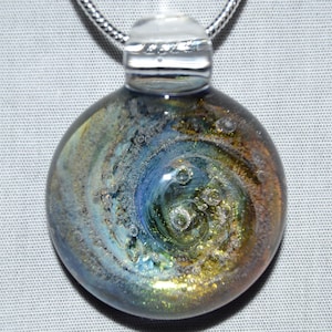 May include: A round glass pendant with a silver chain. The glass is a swirling mix of blue, green, and gold with small air bubbles trapped inside.