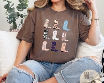 May include: A brown t-shirt with a graphic of nine different cowboy boots in various colors and patterns. The boots are arranged in three rows of three. The t-shirt is being worn by a person with long brown hair. The text "Espresso" is visible in the upper right corner of the image.