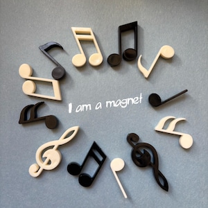 Könnte beinhalten: Eine Anordnung von schwarzen und cremefarbenen Notenmagneten auf grauem Hintergrund. Der Text "I am a magnet" ist in Weiß geschrieben. Die Noten umfassen Viertelnoten, Achtelnoten und Violinschlüssel-Symbole.