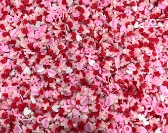 May include: A large assortment of pink and red heart-shaped sprinkles with the word "LOVE" printed on some of the sprinkles.