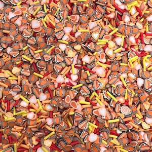 May include: A variety of colorful sprinkles in the shape of hearts, pie slices, and sticks. The sprinkles are a mix of orange, yellow, and red.