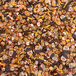 May include: A variety of fall-themed sprinkles in orange, brown, and yellow. The sprinkles include leaves, pumpkins, swirls, and other shapes.