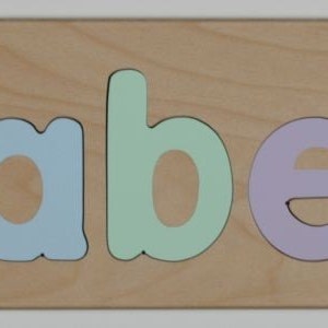 May include: A wooden puzzle with the name "Isabella" spelled out in colorful letters. The letters are pink, yellow, blue, green, purple, and yellow.