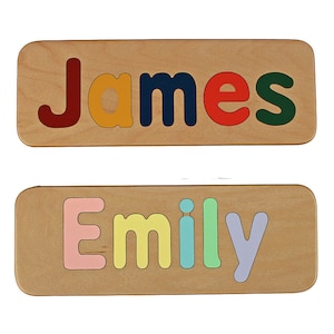 May include: Two wooden puzzle pieces with the names "James" and "Emily" spelled out in colourful letters. The letters are cut out and fit into the puzzle pieces.