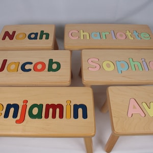 May include: Six wooden children's step stools with names spelled out in colorful puzzle pieces. The names are Noah, Charlotte, Jacob, Sophia, Benjamin, and Ava.
