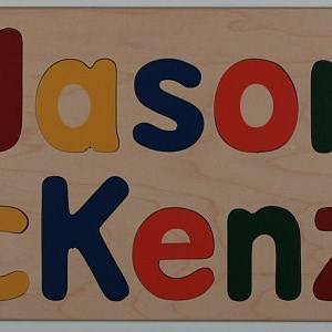 May include: A personalised wooden puzzle featuring the name "Jason McKenzie" in colourful letters. The puzzle includes a train and aeroplane cutout.