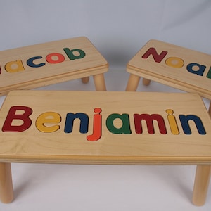 Puede incluir: Tres taburetes de madera con los nombres "Jacob", "Noah" y "Benjamin" escritos en letras de colores en la parte superior.