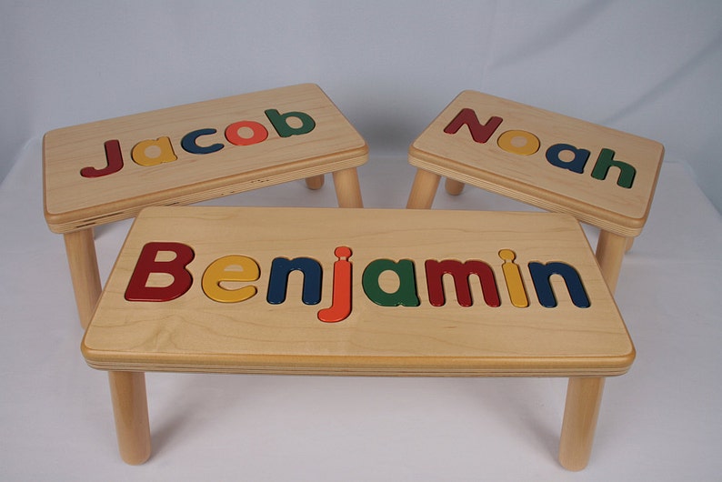 Puede incluir: Tres taburetes de madera con los nombres "Jacob", "Noah" y "Benjamin" escritos en letras de colores en la parte superior.