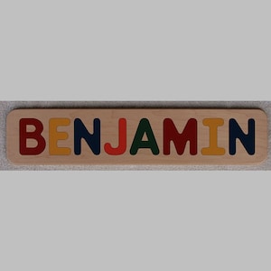 May include: Wooden puzzle with the name "BENJAMIN" spelled out in colorful letters. The letters are red, yellow, blue, red, green, red, yellow, and blue.