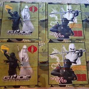 May include: Fabric panel featuring four squares with G.I. Joe characters. Each square has a green camouflage background. The top left and bottom left squares show the text "G.I. Joe The Rise of Cobra" with two characters. The top right and bottom right squares show the text "Snake Eyes" and "Storm Shadow".