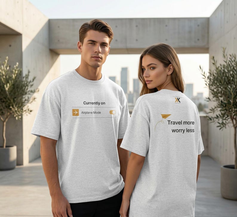 May include: Two people wearing light gray t-shirts. The front of the first shirt has the text "Currently on Airplane Mode" with a graphic. The second shirt has a paper airplane graphic and the text "Travel more worry less".