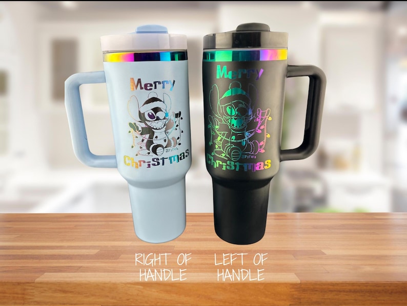 May include: Two stainless steel travel mugs with handles. The mug on the left is black with a rainbow iridescent finish and the mug on the right is light blue with a rainbow iridescent finish. Both mugs feature a cartoon character with the text "Merry Christmas".