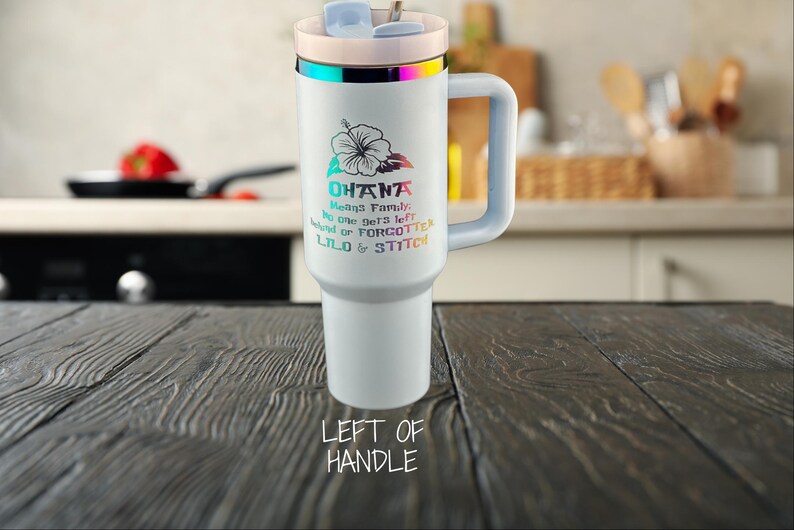 May include: White travel mug with a rainbow iridescent lid and handle. The mug has a floral design and the text "Ohana means family. No one gets left behind or forgotten. Lilo & Stitch".