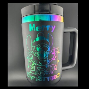 May include: Black travel mug with a rainbow iridescent band around the top. The mug has a handle and features a graphic of Stitch from Lilo & Stitch wearing a Santa hat and holding Christmas lights. The text "Merry Christmas" is printed on the mug.