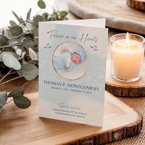 May include: A memorial card with the text "Forever in our Hearts" and a photo of a baby. The card includes the name "Thomas P. Montgomery" and dates. A lit candle sits nearby on a wooden surface.