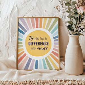Peut inclure: Une affiche encadrée avec un cadre doré présente un motif d'éclat de soleil coloré aux teintes pastel. Le texte central dit "Never forget the DIFFERENCE you have made." Un vase blanc avec des fleurs est à côté de l'affiche.