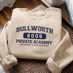 Könnte beinhalten: Beiges Sweatshirt mit Rundhalsausschnitt und marineblauem Text: "BULLWORTH 2006 PRIVATE ACADEMY BULLWORTH • NEW HAMPSHIRE". Das Sweatshirt ist gefaltet, die Ärmel und der Kragen sind sichtbar.