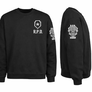 May include: Black crewneck sweatshirt with white graphics. The front features "R.P.D." and a star emblem. The sleeve displays a badge with text "R.P.D. OFFICER TRAINING ACADEMY". The sweatshirt is shown from the front and side.