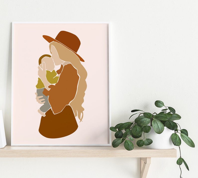 May include: Abstract art print featuring a mother and child in warm earth tones. The mother wears a brown hat and dress, holding the child in a tender embrace. The background is a soft pink, creating a minimalist and modern aesthetic. The artwork is framed in white.