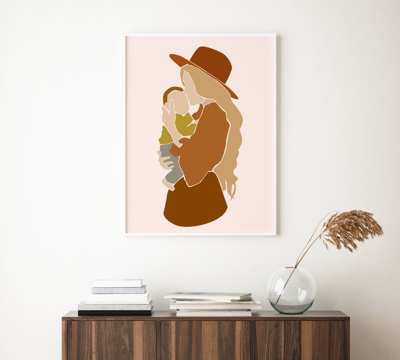 May include: Abstract art print featuring a mother and child in warm earth tones. The artwork depicts a woman in a brown hat and dress holding a child. The background is a soft pink, and the print is framed in white.