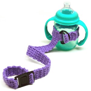 May include: A purple crocheted strap with a black buckle attached to a turquoise plastic sippy cup with two handles.