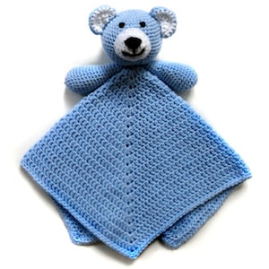 Peut inclure: Une couverture pour bébé en crochet bleu clair avec un ours en crochet bleu attaché. L'ours a des oreilles blanches, un nez blanc et des yeux noirs.