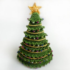 Puede incluir: Un árbol de Navidad de crochet verde con una estrella amarilla en la parte superior. El árbol está decorado con cuentas de colores y cuerda dorada.