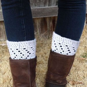 May include: White crocheted boot cuffs with a lacy pattern. The cuffs are worn over brown suede boots and blue jeans.