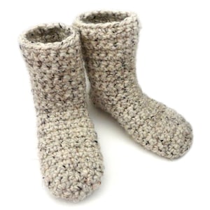 May include: A pair of crocheted slipper socks in a beige and white speckled yarn. The socks are made with a simple stitch pattern and have a soft, cozy look.