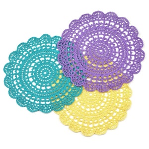 May include: Three crocheted doilies in purple, teal, and yellow. The doilies are layered on top of each other.