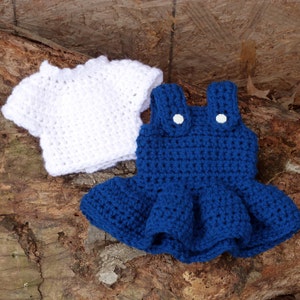 May include: A white crocheted shirt and a blue crocheted overall dress with white buttons. The dress has a ruffled skirt.