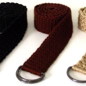 May include: Three crocheted belts with metal D-rings. The belts are black, brown, and beige.