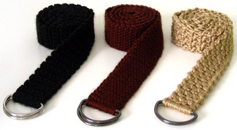 May include: Three crocheted belts with metal D-rings. The belts are black, brown, and beige.