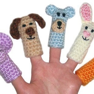 May include: A hand displays five colorful, crocheted finger puppets. The puppets are shaped like a purple elephant, a tan dog, a light blue bear, a white bunny with pink ears, and an orange fox. Each puppet has a smiling face.