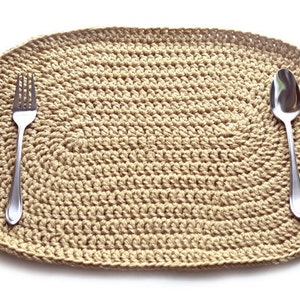 Puede incluir: Un mantel individual ovalado de crochet beige con un tenedor y una cuchara de plata en la parte superior.