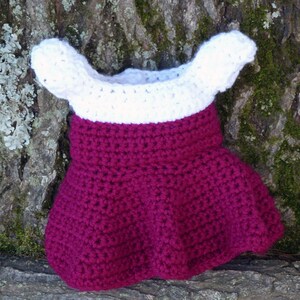May include: A crocheted dress with a white top and a burgundy skirt. The dress is made with a simple stitch and has a ruffled hem.