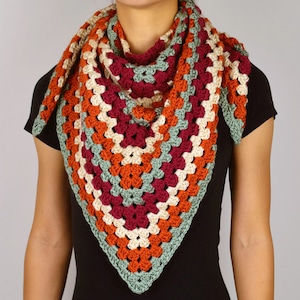 May include: A crocheted triangular scarf with a multi-colored granny square pattern in shades of green, orange, cream, and burgundy.