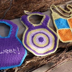 May include: Three crocheted baby bibs in purple, yellow, and orange with blue accents. The purple bib has the word "Sweet!" embroidered on it.