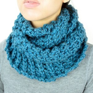 May include: A teal blue knitted cowl neck scarf. The scarf is thick and textured, and it is folded over to create a cowl neck effect.