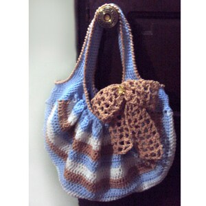 May include: A handmade crochet bag in shades of light blue, white, and brown. The bag features a striped pattern and a matching crochet bow. The bag is hanging from a gold-colored knob.